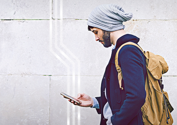 man on street in front of a wall looking at his smartphone